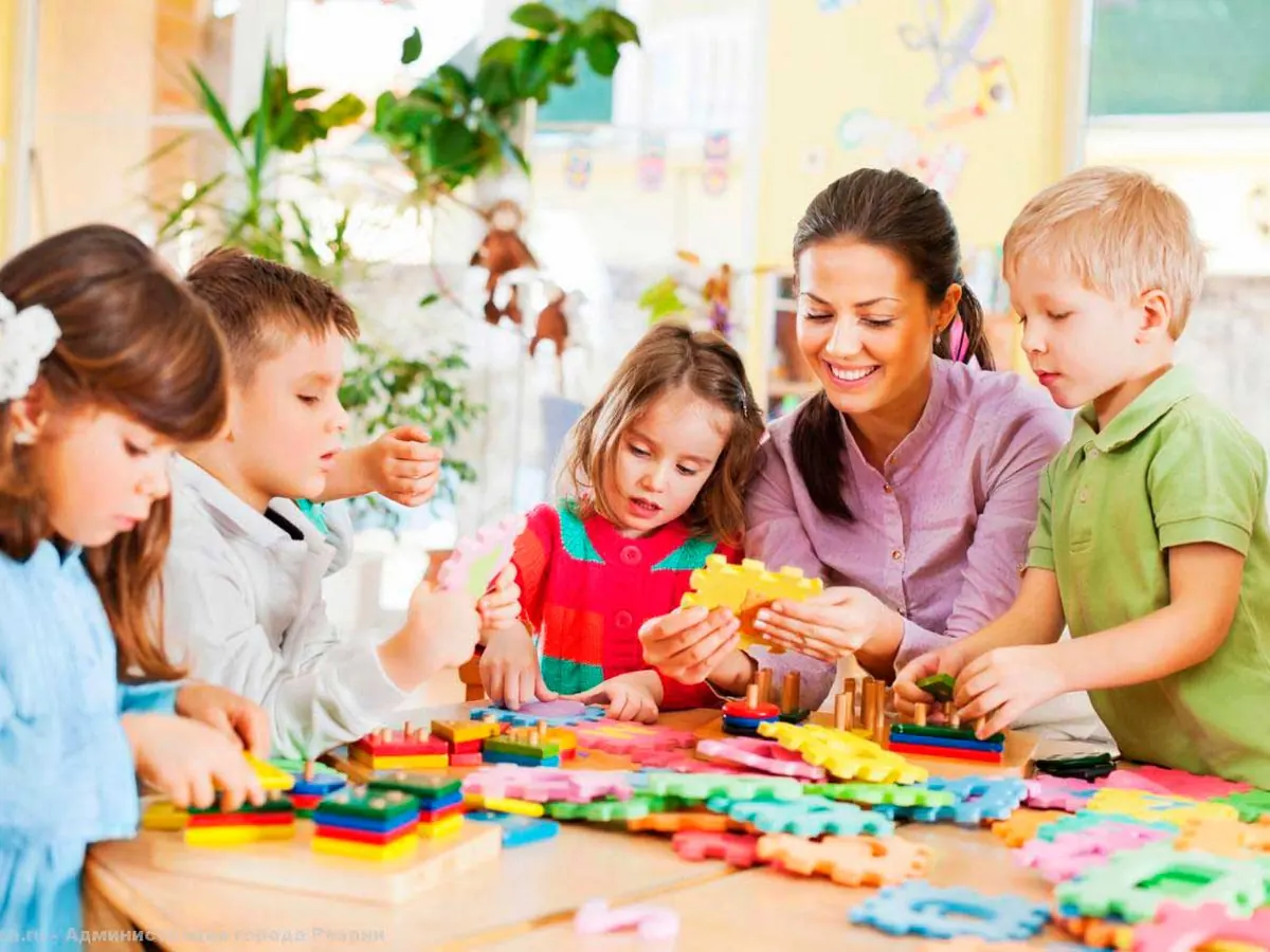 Niños de preescolar armando figuras de colores junto a su maestra